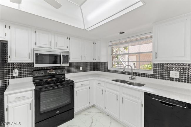 Kitchen featuring white cabinets, light tile patterned floors, black appliances, and sink | Image 33