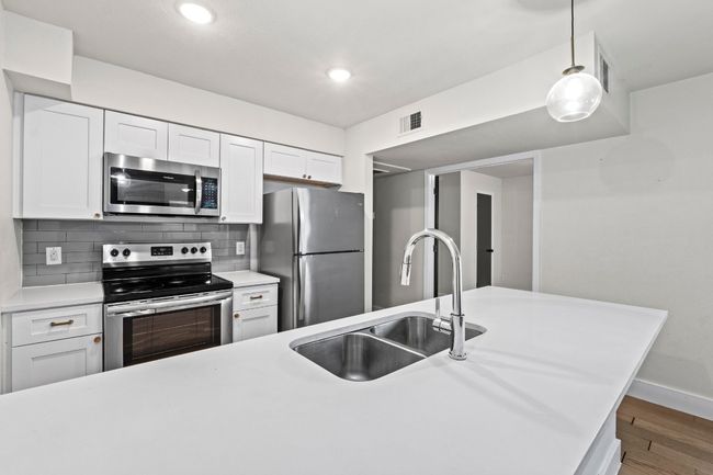 Kitchen with stainless steel appliances, a sink, wood finished floors, light countertops, and recessed lighting | Image 14
