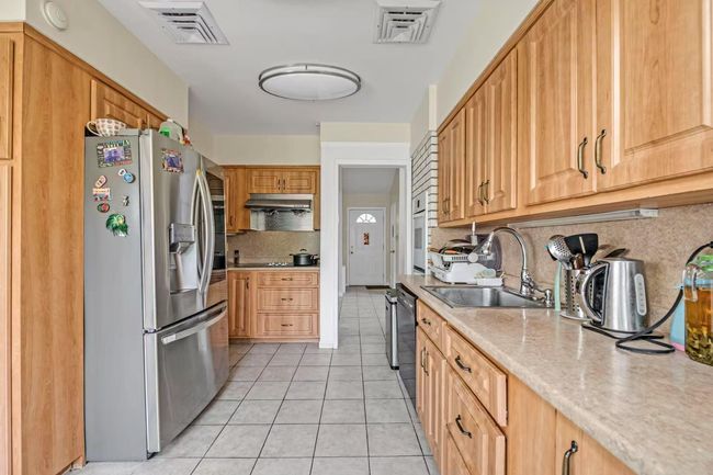 Kitchen featuring stainless steel fridge with ice dispenser, decorative backsplash, light tile patterned flooring, black dishwasher, and under cabinet range hood | Image 5