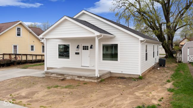 bungalow-style home featuring central air condition unit, an outdoor structure, a patio area, a shingled roof, and a storage unit | Image 4