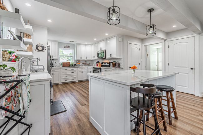 Kitchen featuring stainless steel appliances, backsplash, light wood-style floors, a kitchen bar, and white cabinetry | Image 10