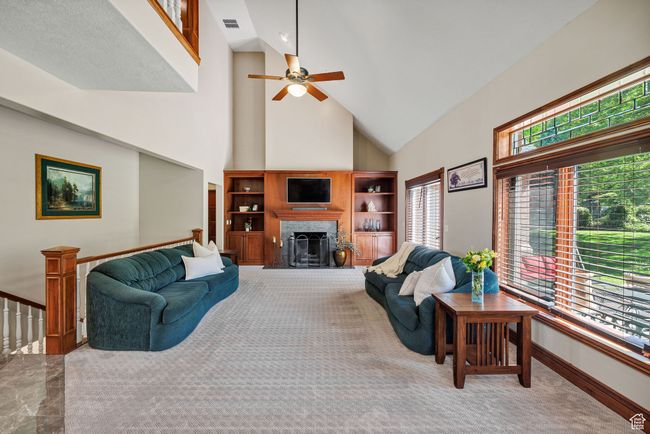 Carpeted living room featuring high vaulted ceiling, a ceiling fan, and a fireplace | Image 22
