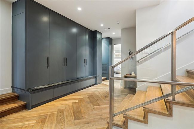 This multi-functional hallway is more than just a transition space—it’s a thoughtfully designed connector between the main living/kitchen area, additional rooms on this floor, and the stairway leading to both upper and lower levels. Custom built-in lockers offer a stylish and practical drop zone for coats, backpacks, briefcases, and purses—keeping the home organized and clutter-free. To the right of the accent table, you’ll find the laundry room—right where it makes the most sense for daily living. | Image 14