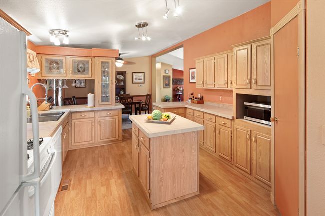 Kitchen featuring light countertops, light brown cabinetry, light wood-style floors, a kitchen island, and white appliances | Image 18
