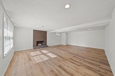 Unfurnished living room featuring a textured ceiling, brick wall, light hardwood / wood-style floors, and a brick fireplace | Image 2