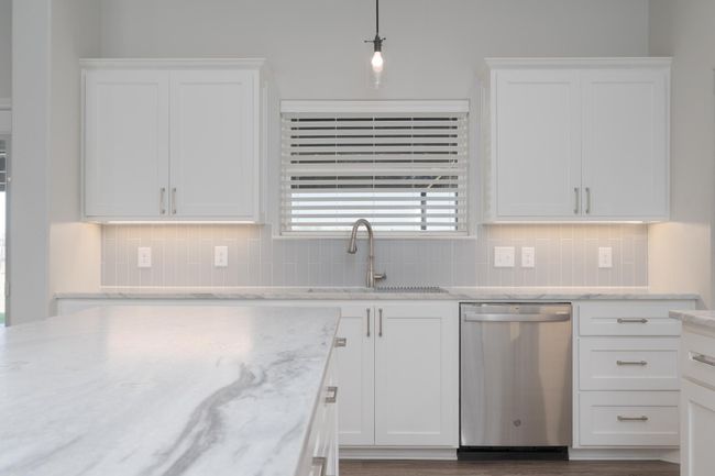 Kitchen featuring stainless steel dishwasher, tasteful backsplash, white cabinetry, and a sink | Image 11