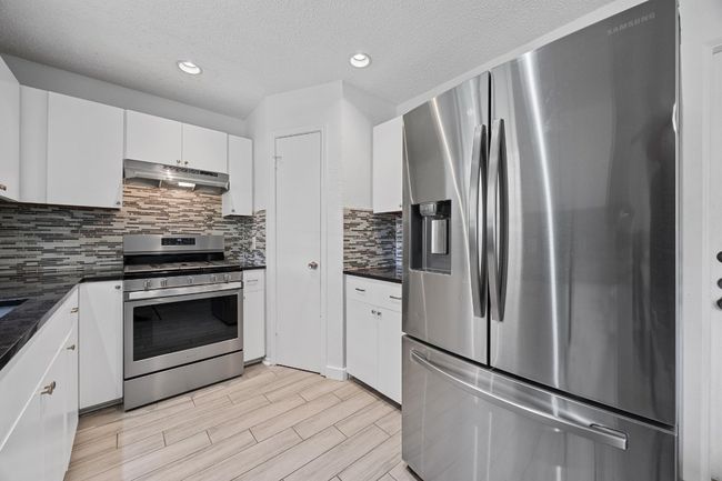 Kitchen with dark countertops, white cabinetry, decorative backsplash, under cabinet range hood, and appliances with stainless steel finishes | Image 4