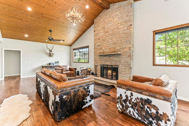 Living area with wood-type flooring, a stone fireplace, wood ceiling with exposed beams, baseboards, and high vaulted ceiling | Image 4