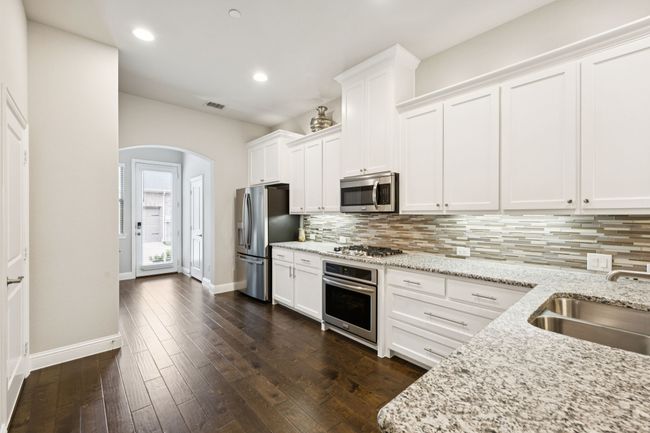 Kitchen featuring appliances with stainless steel finishes, arched walkways, decorative backsplash, white cabinets, and recessed lighting | Image 7