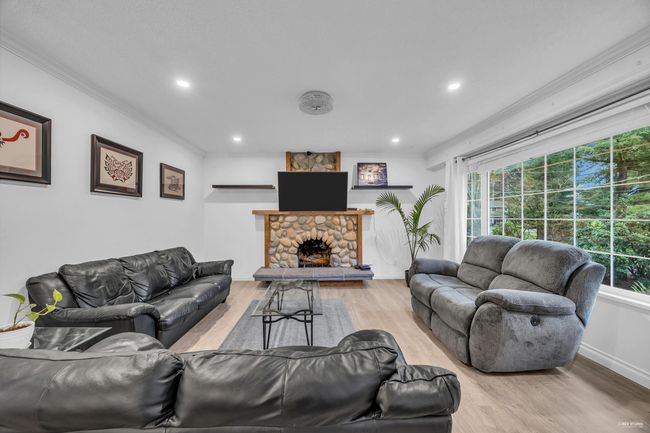 Living room featuring ornamental molding, healthy amount of natural light, wood finished floors, recessed lighting, and a stone fireplace | Image 6