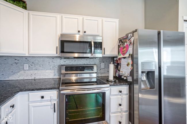 kitchen featuring dark stone countertops, white cabinets, stainless steel appliances, and decorative backsplash | Image 15