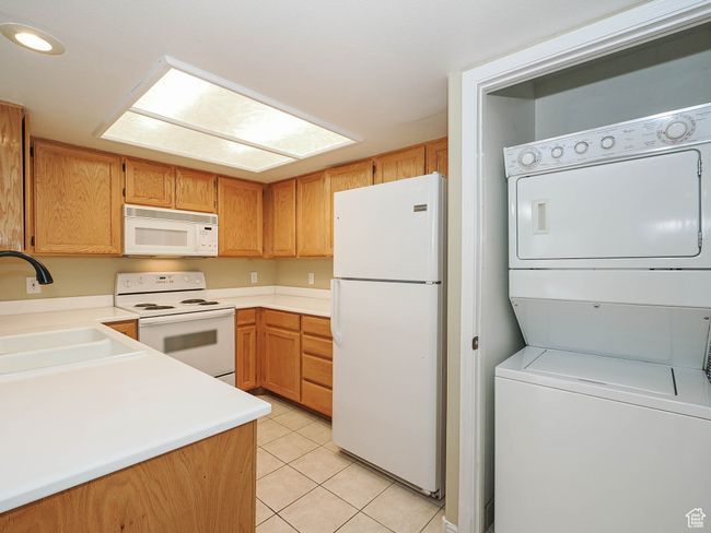 Kitchen with a sink, white appliances, light tile patterned floors, light countertops, and stacked washer and clothes dryer | Image 9