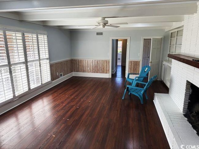 Unfurnished room featuring beamed ceiling, built in shelves, ceiling fan, a fireplace, and dark hardwood / wood-style flooring | Image 11