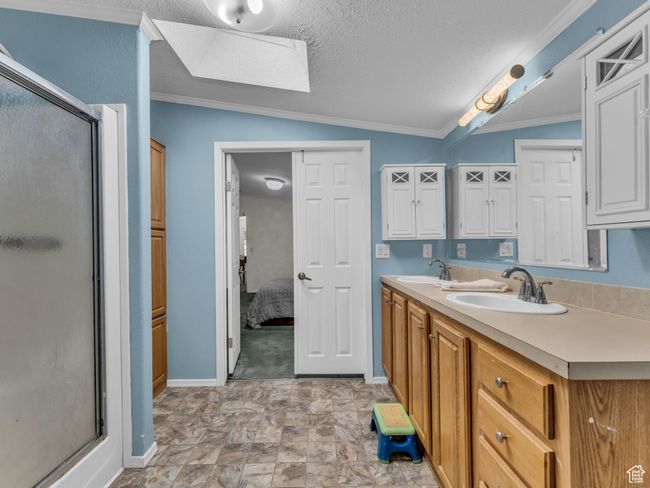 Primary bathroom featuring a shower stall, baseboards, double vanity, a textured ceiling, and vaulted ceiling | Image 14