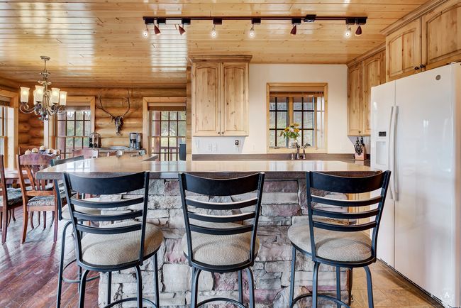 Kitchen with white refrigerator with ice dispenser, wooden ceiling, log walls, a chandelier, and light brown cabinetry | Image 13