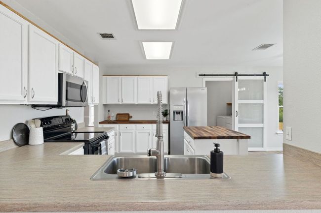 Kitchen featuring appliances with stainless steel finishes, butcher block countertops, a sink, a barn door, and white cabinets | Image 14