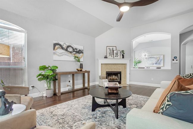 Living room with wood finished floors, a ceiling fan, vaulted ceiling, baseboards, and a fireplace | Image 4