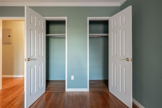 Unfurnished bedroom featuring baseboards, electric panel, crown molding, multiple closets, and wood finished floors | Image 11
