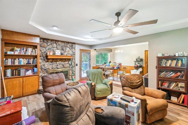 Living room featuring ceiling fan, a tray ceiling, wood finished floors, a chandelier, and a fireplace | Image 11