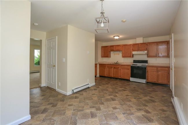 Kitchen with white stove, a baseboard radiator, under cabinet range hood, and baseboards | Image 4
