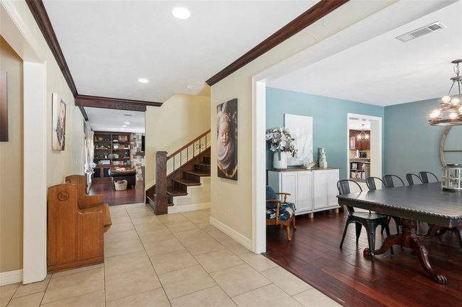 This inviting home features a spacious entryway with tiled flooring leading to a cozy living area with wooden floors. A dining room with a stylish chandelier and ample natural light is adjacent, alongside a staircase with elegant railing. | Image 9