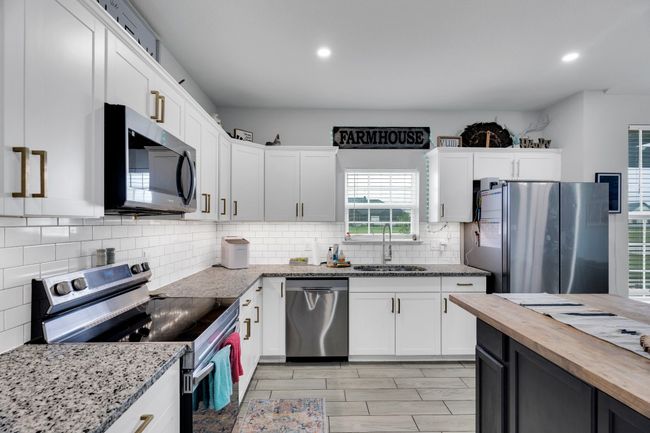 Kitchen with stainless steel appliances, a sink, butcher block counters, recessed lighting, and white cabinets | Image 11