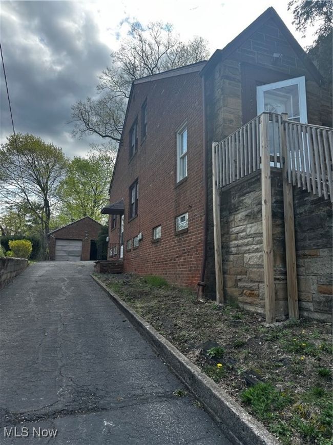 View of property exterior featuring driveway, an outdoor structure, a detached garage, and brick siding | Image 4