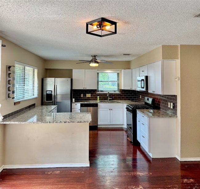 Kitchen featuring stainless steel appliances, light stone countertops, dark wood finished floors, decorative backsplash, and a peninsula | Image 6