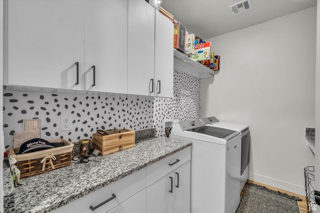 Clothes washing area with wood finished floors, washing machine and clothes dryer, baseboards, visible vents, and cabinet space | Image 24