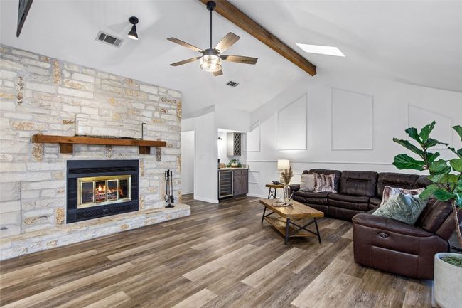 Living room with wine cooler, ceiling fan, wood finished floors, a stone fireplace, and a skylight | Image 10