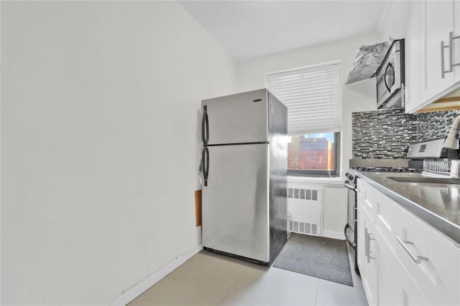 Kitchen featuring appliances with stainless steel finishes, radiator, decorative backsplash, and white cabinetry | Image 9
