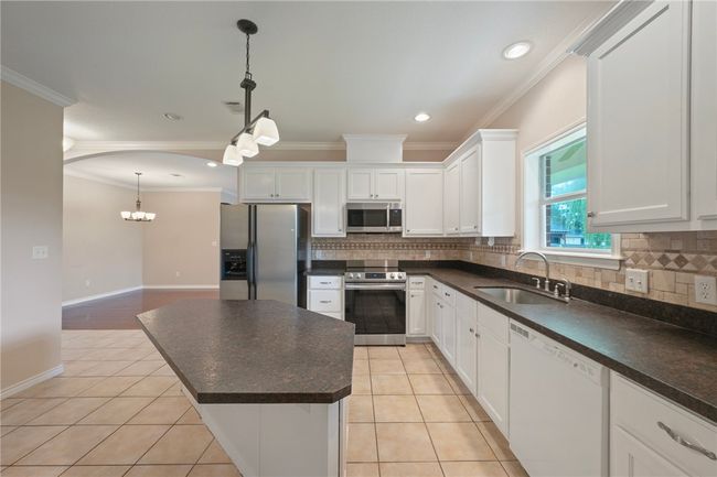 Kitchen featuring appliances with stainless steel finishes, a sink, crown molding, dark countertops, and a chandelier | Image 8