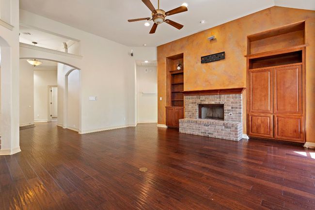 Unfurnished living room with built in features, arched walkways, ceiling fan, and dark wood-style flooring | Image 7