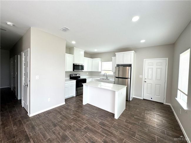 Kitchen featuring stainless steel appliances, a sink, baseboards, white cabinets, and light countertops | Image 4