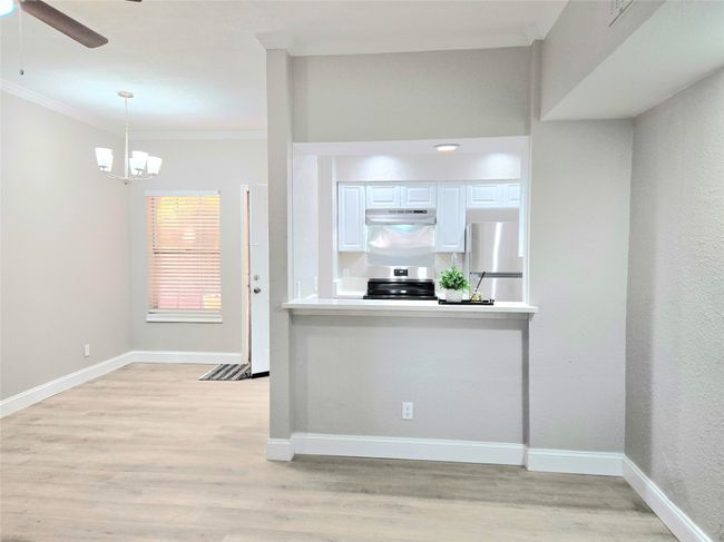 Kitchen featuring stainless steel appliances, crown molding, white cabinetry, light wood-style flooring, and under cabinet range hood | Image 7