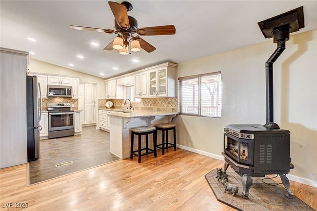 Kitchen with appliances with stainless steel finishes, a wood stove, a peninsula, light stone counters, and a kitchen bar | Image 17