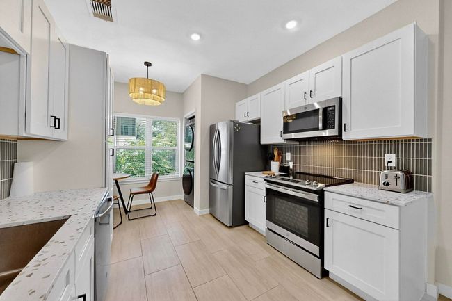 Kitchen featuring stainless steel appliances, stacked washer / dryer, backsplash, white cabinetry, and recessed lighting | Image 13