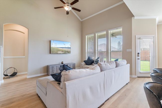 Living room with ornamental molding, light wood-type flooring, ceiling fan, high vaulted ceiling, and baseboards | Image 7