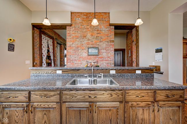 kitchen featuring brown cabinetry, brick wall, a sink, and hanging light fixtures | Image 23