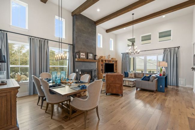 Dining area featuring light wood finished floors, a towering ceiling, a chandelier, a tile fireplace, and beamed ceiling | Image 19