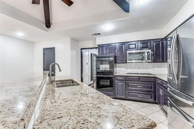 Kitchen with light stone counters, light tile patterned floors, visible vents, appliances with stainless steel finishes, and a sink | Image 13
