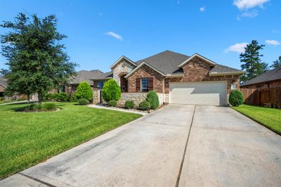 The home exudes a charming curb appeal with its stunning brick and stone exterior accented by neutral trim details and framed by meticulously manicured landscaping and a lush green lawn. | Image 3