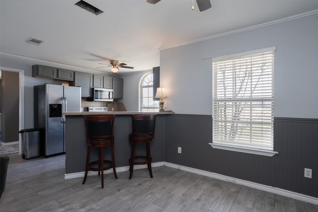 Kitchen featuring a ceiling fan, appliances with stainless steel finishes, wainscoting, crown molding, and a breakfast bar area | Image 15