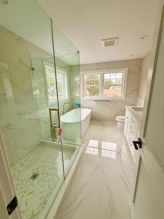Full bathroom with vanity, marble tiled flooring, a marble finish shower, a freestanding bath, and tile walls | Image 6