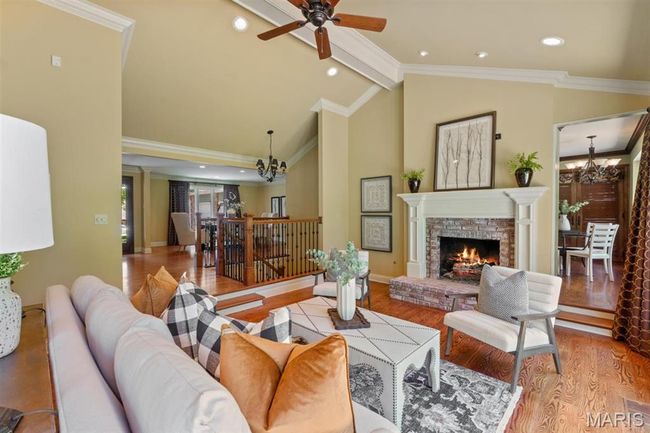 Living area with a chandelier, wood finished floors, beamed ceiling, ornamental molding, and a fireplace | Image 7