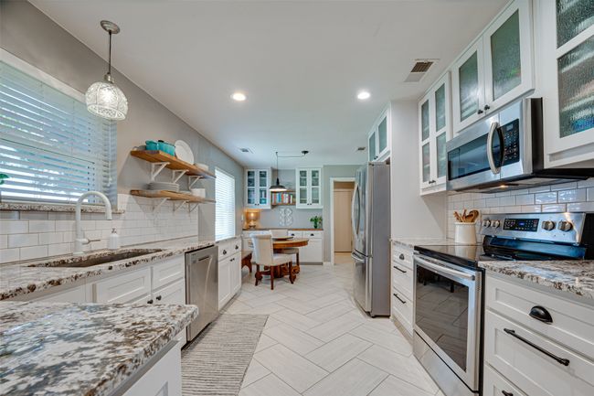 Kitchen with appliances with stainless steel finishes, backsplash, white cabinets, light stone counters, and recessed lighting | Image 13