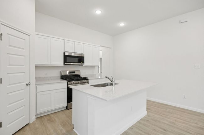 Kitchen featuring stainless steel appliances, light wood-type flooring, a kitchen island with sink, white cabinetry, and light stone countertops | Image 12