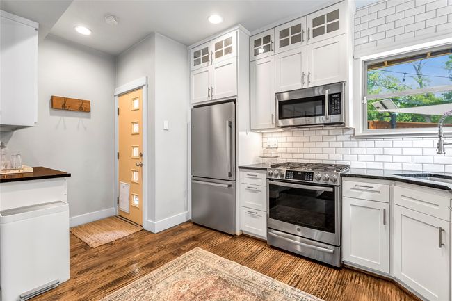 Kitchen featuring appliances with stainless steel finishes, dark countertops, a sink, dark wood-style flooring, and decorative backsplash | Image 9