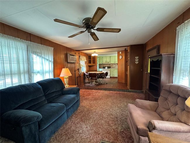 Living area with wood walls, a wall mounted air conditioner, a ceiling fan, and carpet flooring | Image 7