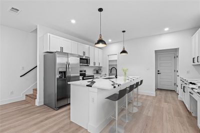 Kitchen featuring a center island with sink, appliances with stainless steel finishes, light stone countertops, white cabinets, and light hardwood / wood-style flooring | Image 3